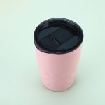 A pink travel tumbler with a black lid, featuring a textured design suitable for beverages.