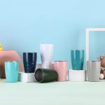A collection of 11 oz. travel tumblers in various colours including teal, navy, pink, white, and grey, displayed on white pedestals.