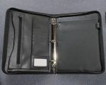 A black ring binder with multiple pockets, a zippered compartment, and a silver metal ring mechanism.