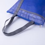 A blue lunch cooler tote with a grey zipper and handles, featuring a textured design. It has a logo on the side.