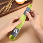 An adjustable measuring spoon in green and grey, with measurement markings, held in two hands against a light background.