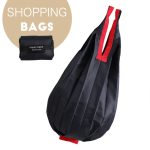 A foldable shopping bag in black with red accents, featuring a handle and a compact, folded design.