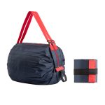 A foldable shopping bag in navy blue with bright red straps, displayed alongside its compact folded form.