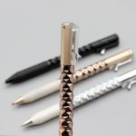 A Crinkle Grip Pen with a textured rose gold grip, alongside black, white, and silver pens, all featuring a clip.