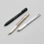 A collection of three Crinkle Grip Pens in black, silver, and white, featuring textured grips and a logo.