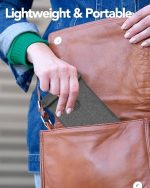 A grey Faraday bag is being placed into a brown leather bag. The background features a denim jacket.