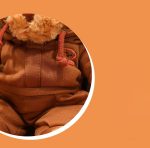 A brown plush teddy bear wearing a matching brown outfit, featuring a small logo on the clothing.
