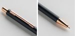 A metal push-up pen in black with a rose gold clip and tip, featuring a textured grip and branding.
