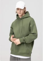 A hooded sweatshirt in olive green, featuring a front kangaroo pocket and drawstrings. The model wears a white cap.