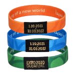 Three elastic wristbands in orange, blue, and green, each featuring a black logo and dates embossed on a label.