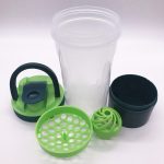 A drink bottle with a transparent body, green lid, and accessories including a storage container and mixing ball.