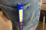 A blue Cob Work Light is clipped onto the back pocket of a pair of denim jeans. The light features a clear lens.