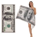 A beach towel featuring a design of a hundred dollar note in green and black tones, held by a model.