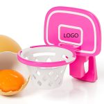 A pink egg yolk separator shaped like a basketball hoop beside a cracked egg with a bright orange yolk.