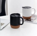 A ceramic mug with a cork base in black and white, featuring a lid, placed beside a laptop on a table.