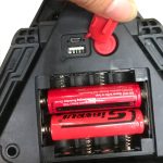 A multifunctional car tool with a red body, displaying battery compartments and charging ports. It features a logo.