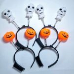 A black headband featuring orange pumpkins and white skulls on springs. Ideal for Halloween celebrations.