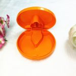 An orange plastic pill cutter and box, featuring a hinged lid and a compartment for pills, set against a soft background.