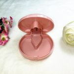 A pink plastic pill cutter and box, featuring a hinged lid and a triangular cutting element inside.