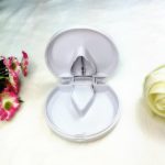 A white plastic pill cutter and pill box with a hinged lid, featuring a central divider inside.
