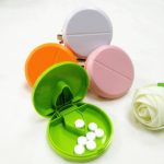 A plastic pill cutter and pill box set in green, orange, pink, and white, featuring compartments for pills.
