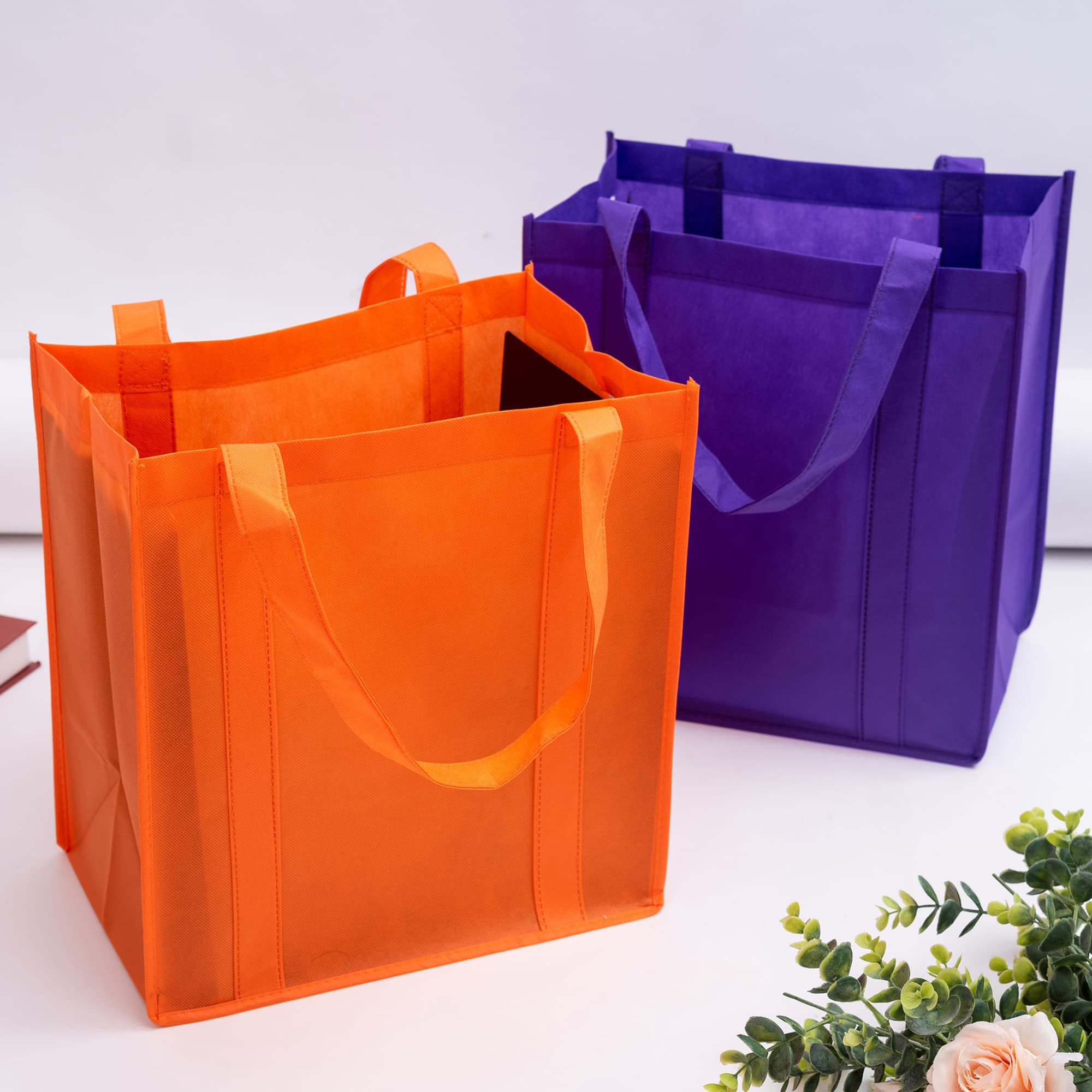 Two reusable shopping bags in vibrant orange and purple, featuring sturdy handles and a structured design. Non Woven Shopping Bag - Image 1