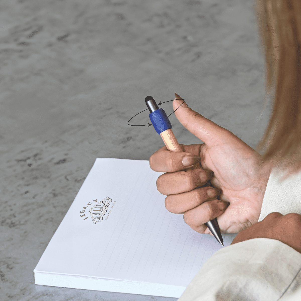 A wooden pen with a blue grip is being held over a blank notepad on a textured surface. Harley Bamboo Spinner Pen - Image 1