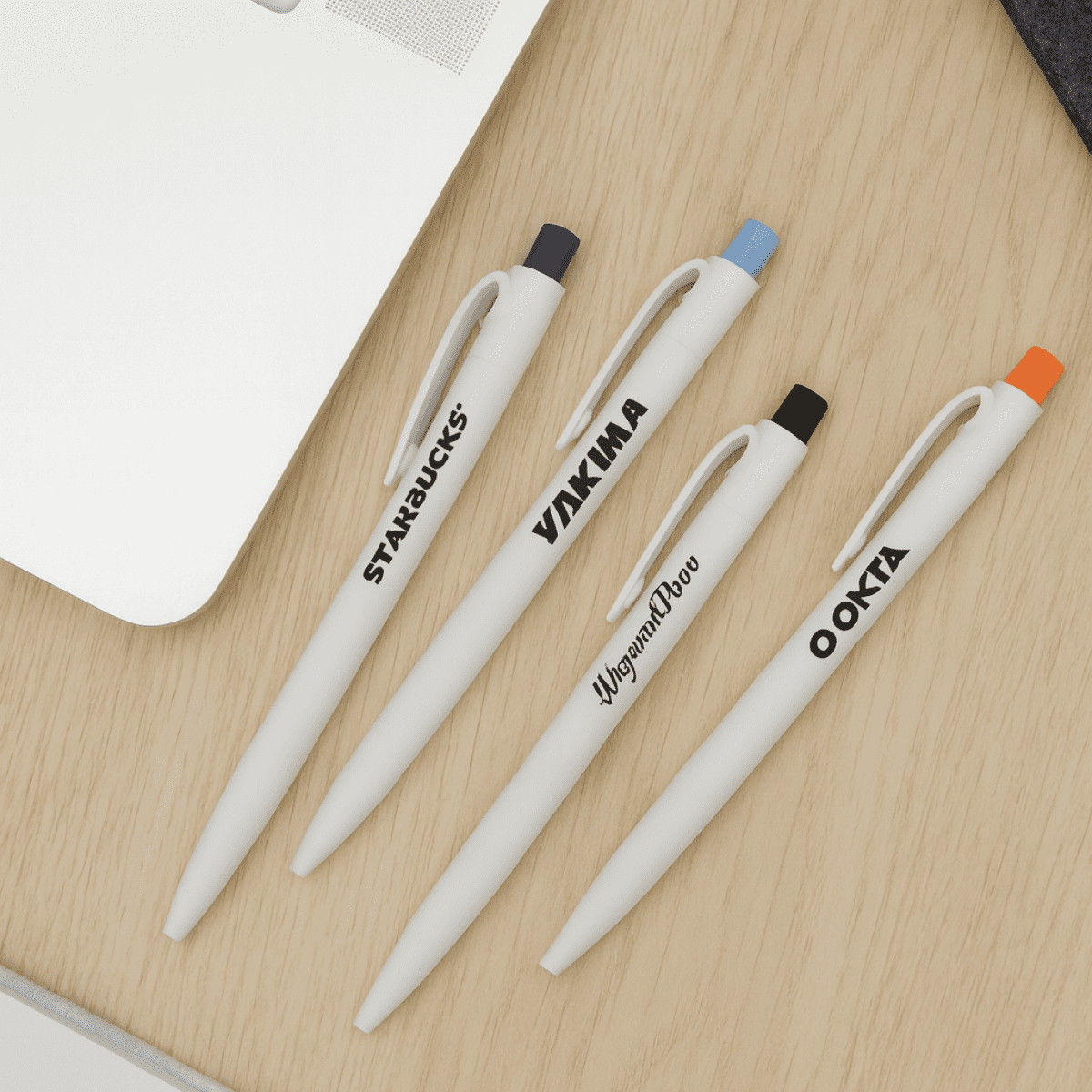 A collection of white plastic pens in black, orange, and blue with various logos on a wooden surface. Sea Shell Pen - Image 1