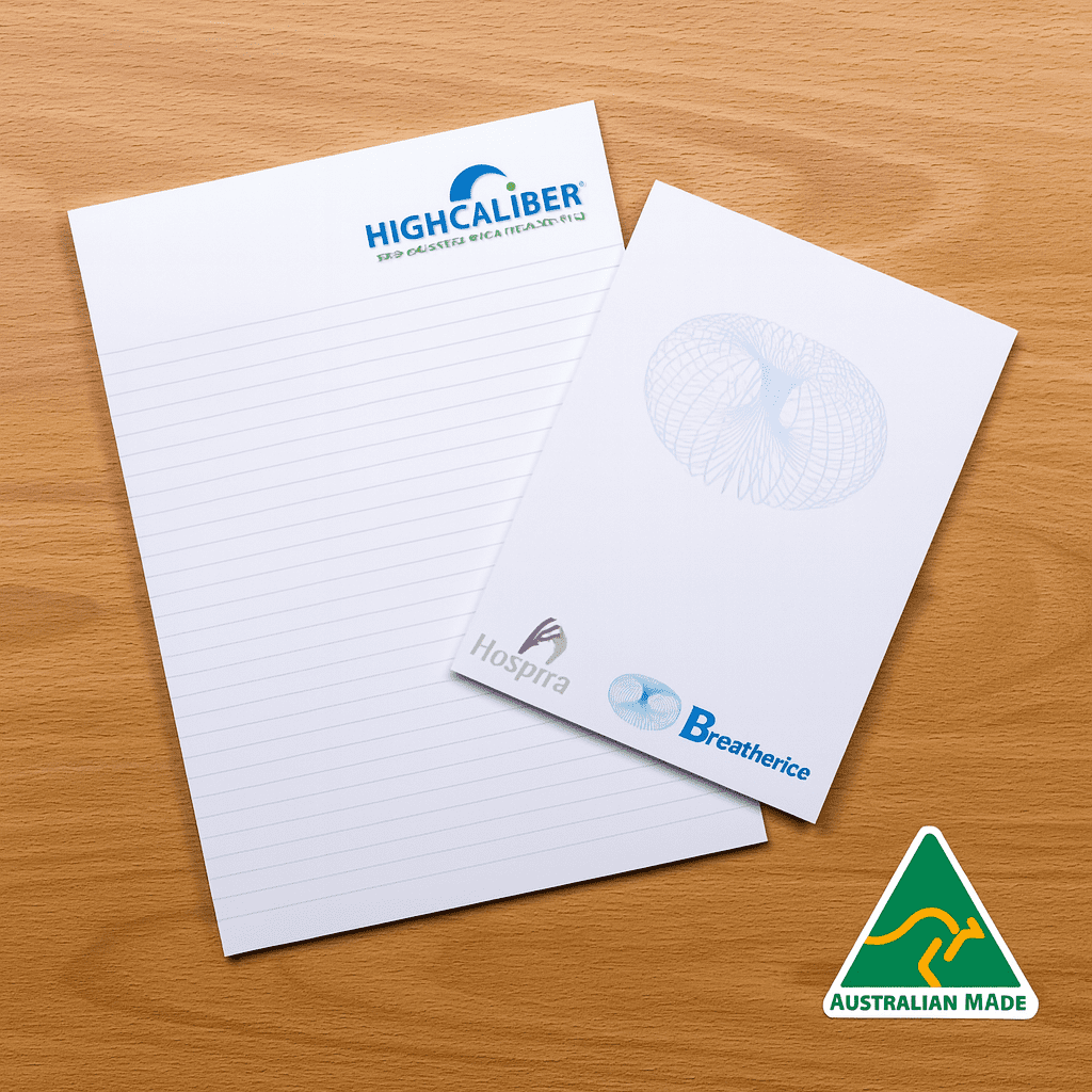 A4 notepad with lined pages, featuring a logo and an Australian Made badge, set on a wooden surface. A4 Note pad (25 leaves per pad) - Image 1