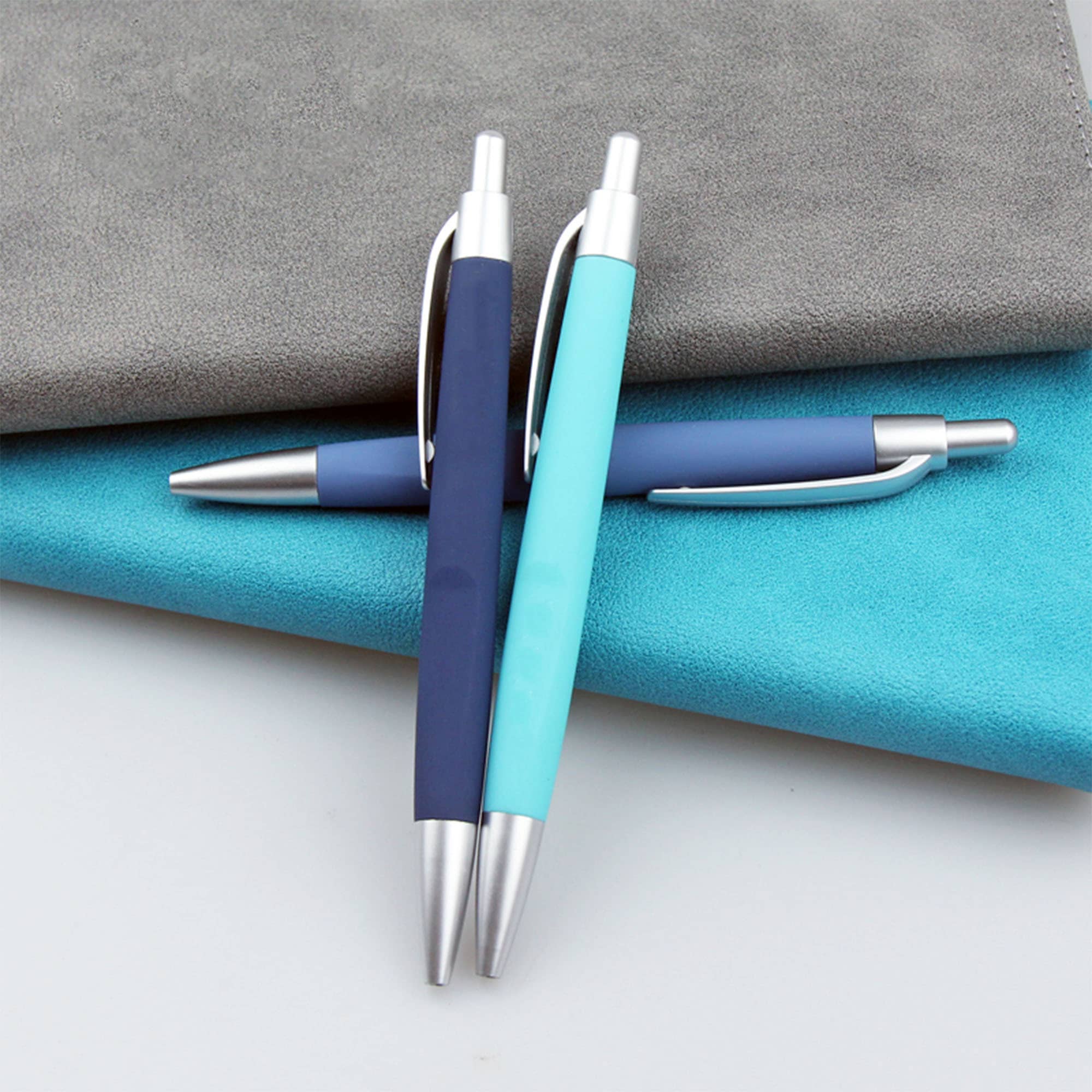 Three plastic pens in navy blue and light blue resting on textured grey and turquoise surfaces, featuring metallic accents. Fiona - Image 1
