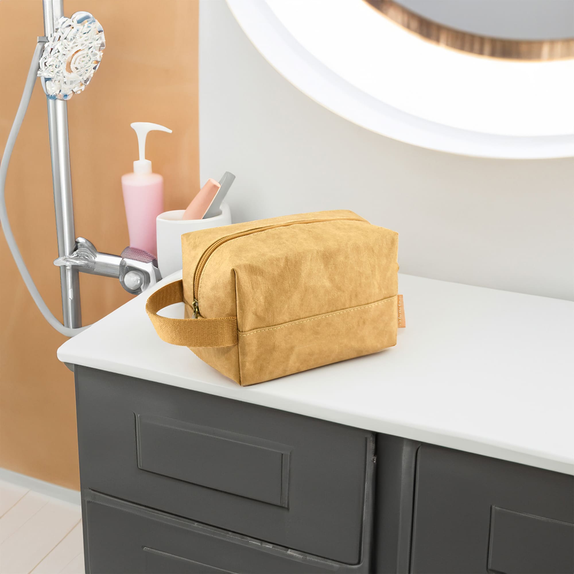 A yellow Kraft paper cosmetic bag with a zip closure, resting on a countertop. It has a handle and a logo. Munro Kraft Paper Cosmetic Bag - Image 1