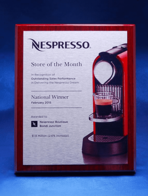 A printed plaque on a veneer timber background featuring a coffee machine and a logo. The plaque has a red border. Printed Plate on Veneer Timber Plaque - Image 1