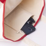 A red and cream canvas tote bag with a zipped pocket containing sunglasses and a mobile phone.