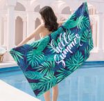 A sublimated beach towel featuring vibrant green leaves on a navy background, with the phrase "hello Summer" and a logo.