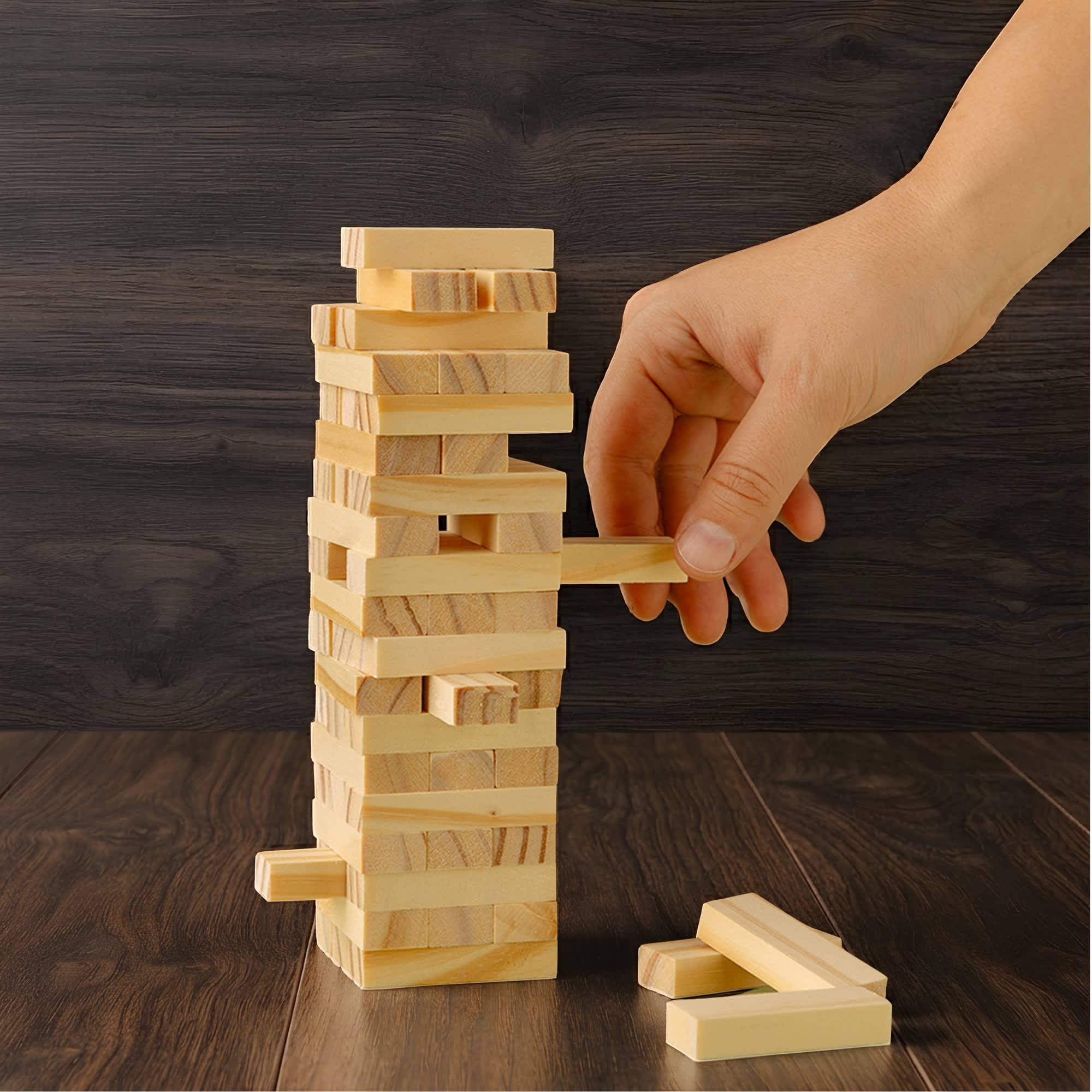 A large wooden tower set featuring light-coloured blocks stacked vertically, with a hand removing a block. Large Wooden Towers Set - Image 1