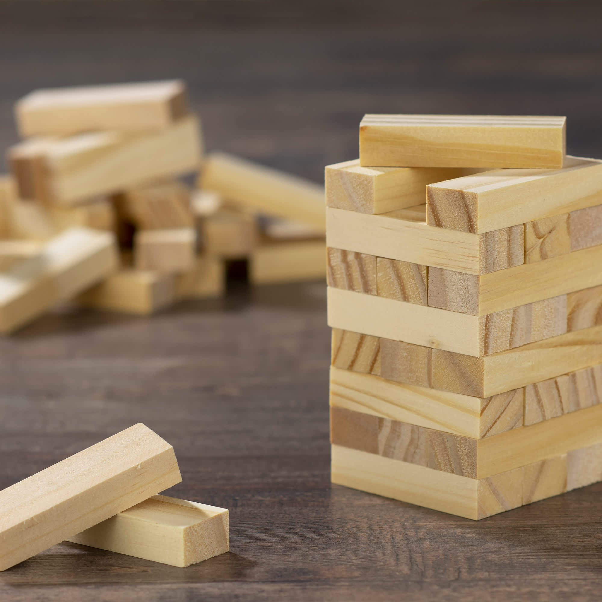 A set of small wooden blocks in light wood tones, stacked to form a tower, with additional blocks scattered nearby. Small Wooden Towers Set - Image 1