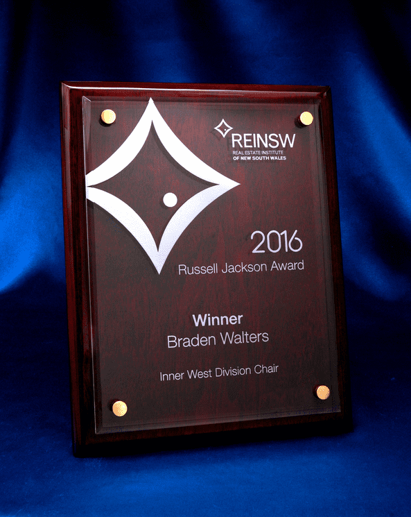 A rosewood plaque featuring a laser-engraved acrylic panel, displaying an award design. It has a glossy finish and gold accents. Piano Finish Rosewood Plaque with Acrylic Panel - Laser Engraved - Image 1
