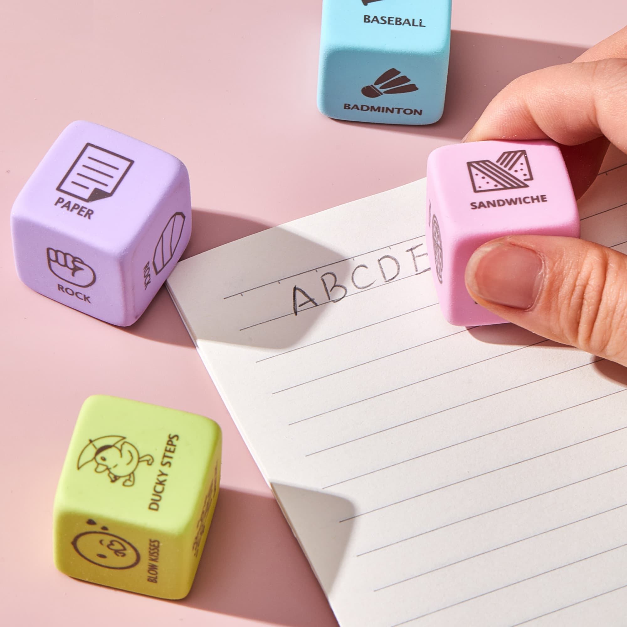 A set of colourful rubber erasers in pastel shades, including purple, pink, and blue, beside a lined notepad. Nero Cube Rubber Eraser - Image 1