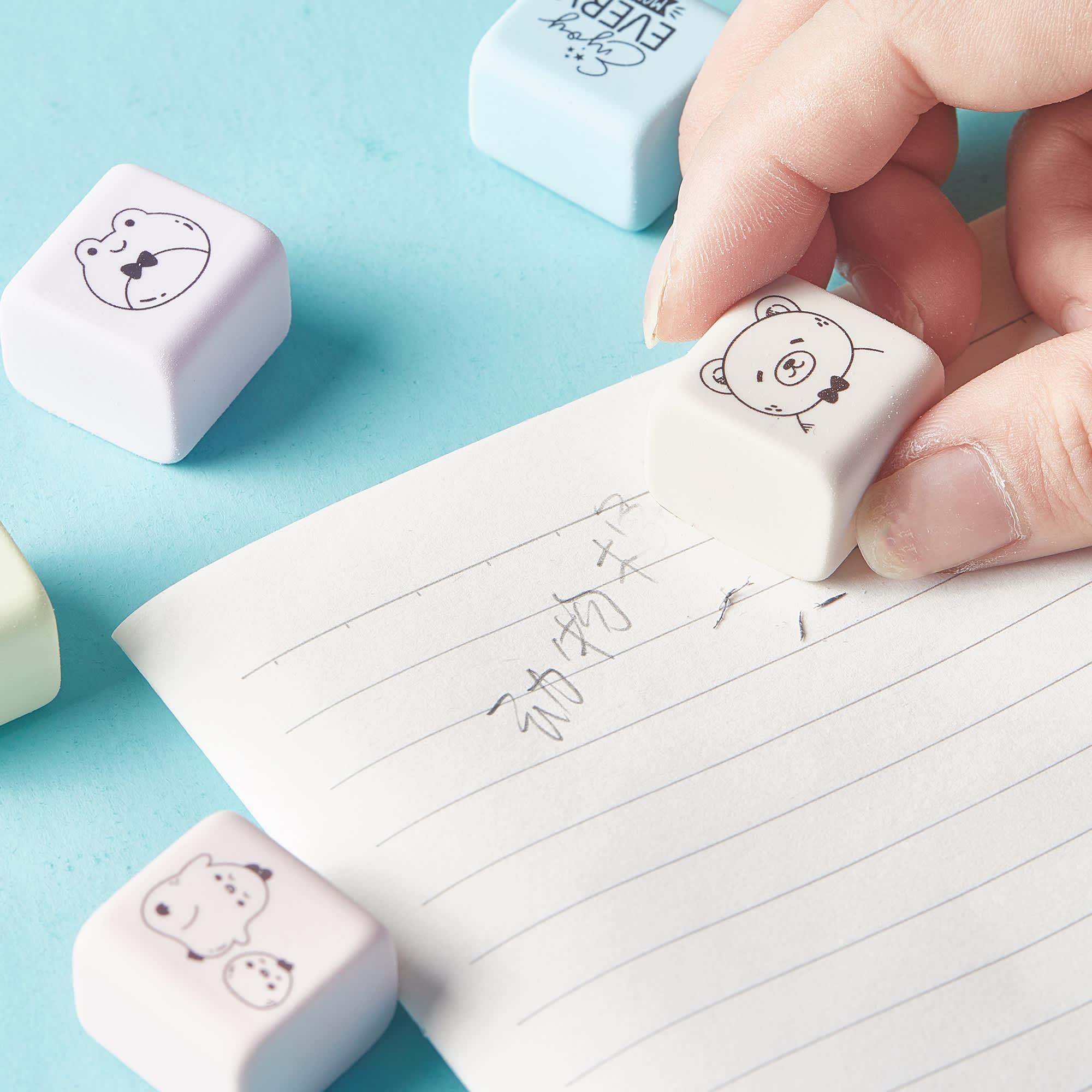 A set of pastel-coloured rubber erasers featuring cute animal designs, being used on lined paper. Happy Cube Rubber Eraser Set - Image 1