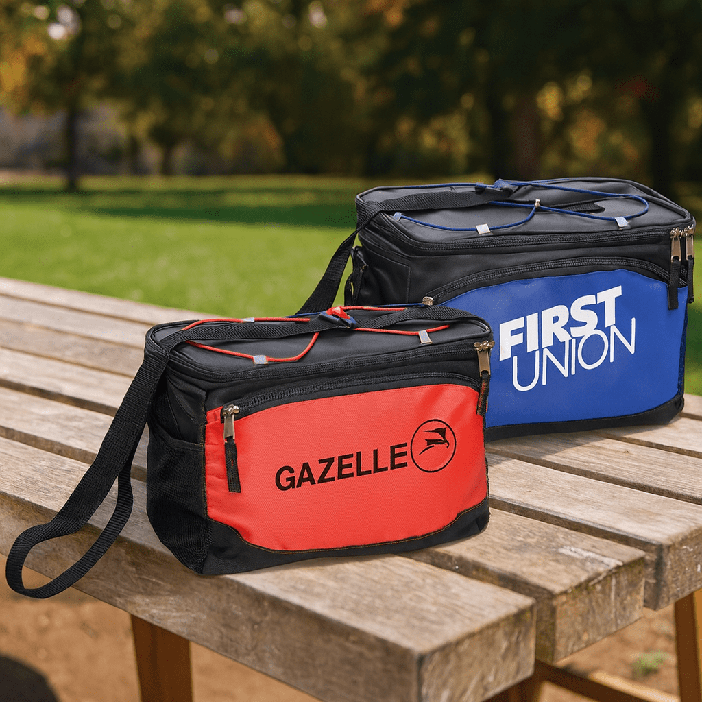 Two cooler bags in red and blue, each with a zipper and a shoulder strap, placed on a wooden table outdoors. 6-Can Cooler Bag - Image 1
