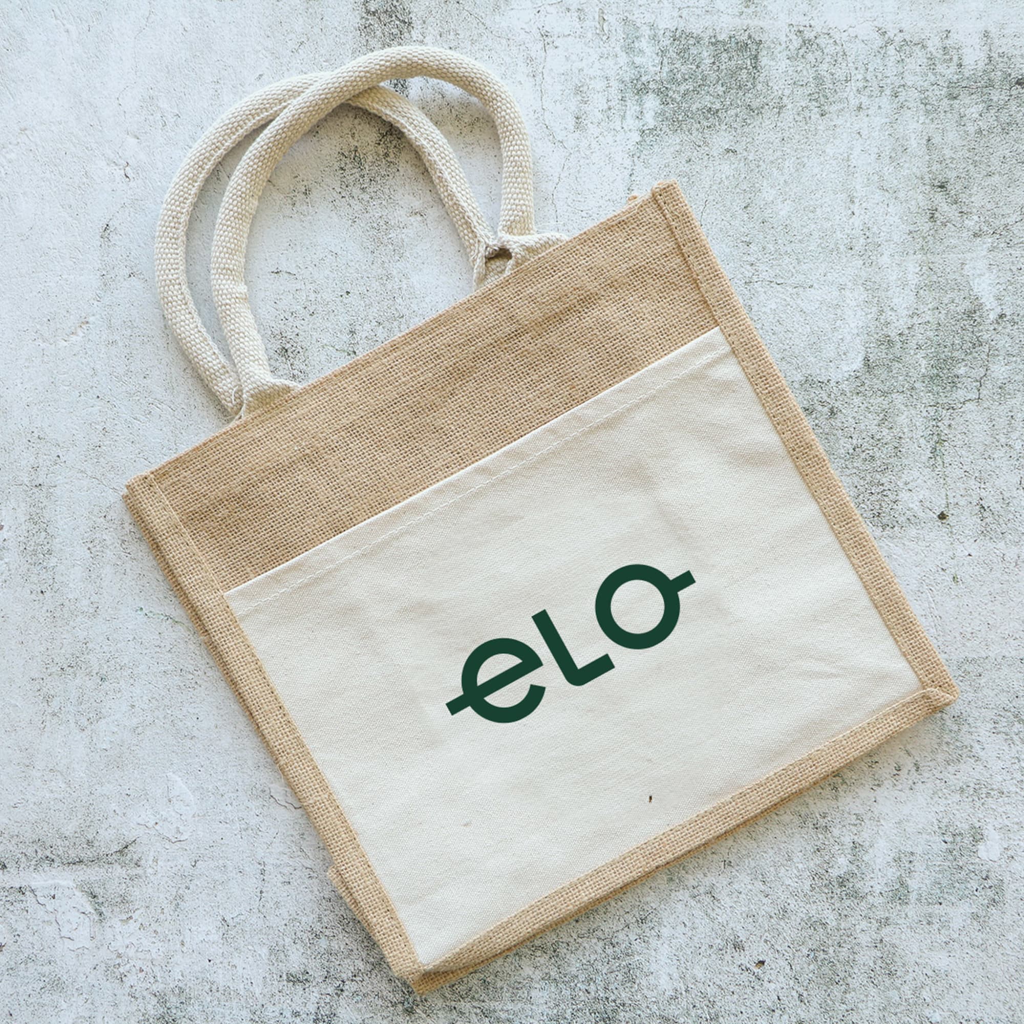 A jute tote bag featuring a natural beige and cream design, with two handles and a visible logo. Jim Jam Jute Tote Bag - Image 1
