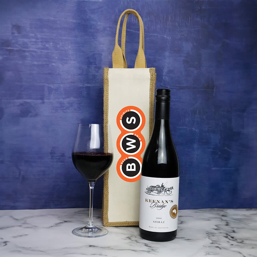 A jute single wine bag in cream with a brown handle, alongside a bottle of red wine and a glass filled with wine. Jute Single Wine Bag - Image 1