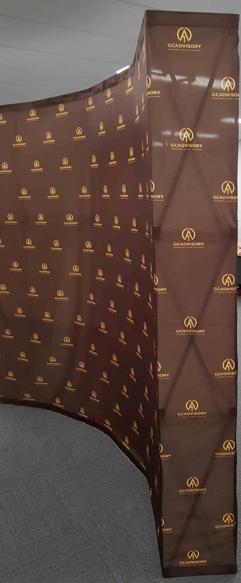 A curved media wall in brown with sides, featuring a repeated logo pattern in gold. Media Wall 3m x 2.25m - Curved -With Sides - Image 1