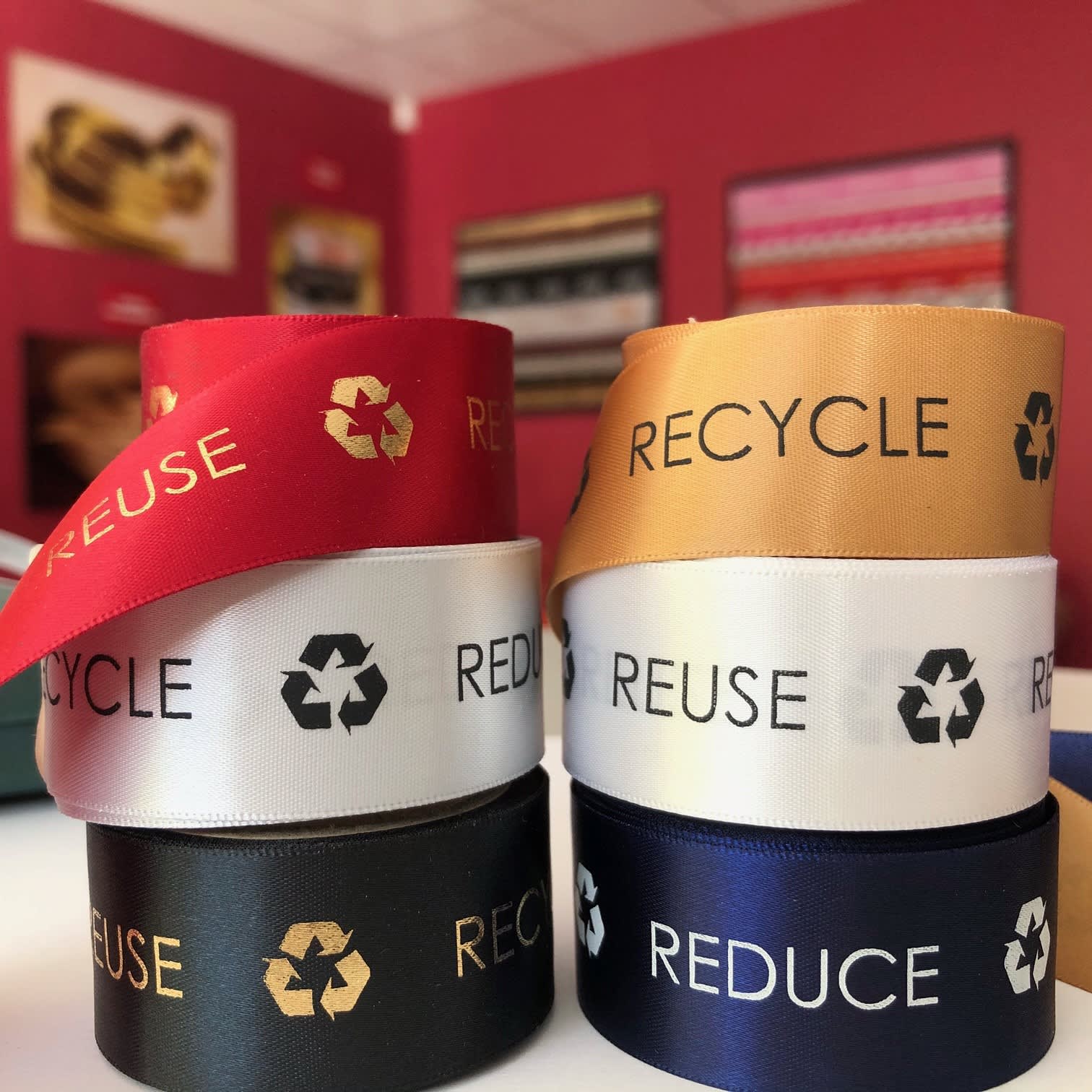 Custom printed recycled woven edge satin ribbons in red, gold, white, black, and navy, featuring eco-friendly logos. Custom Printed Recycled Woven Edge Satin Ribbon 10mm - Image 1