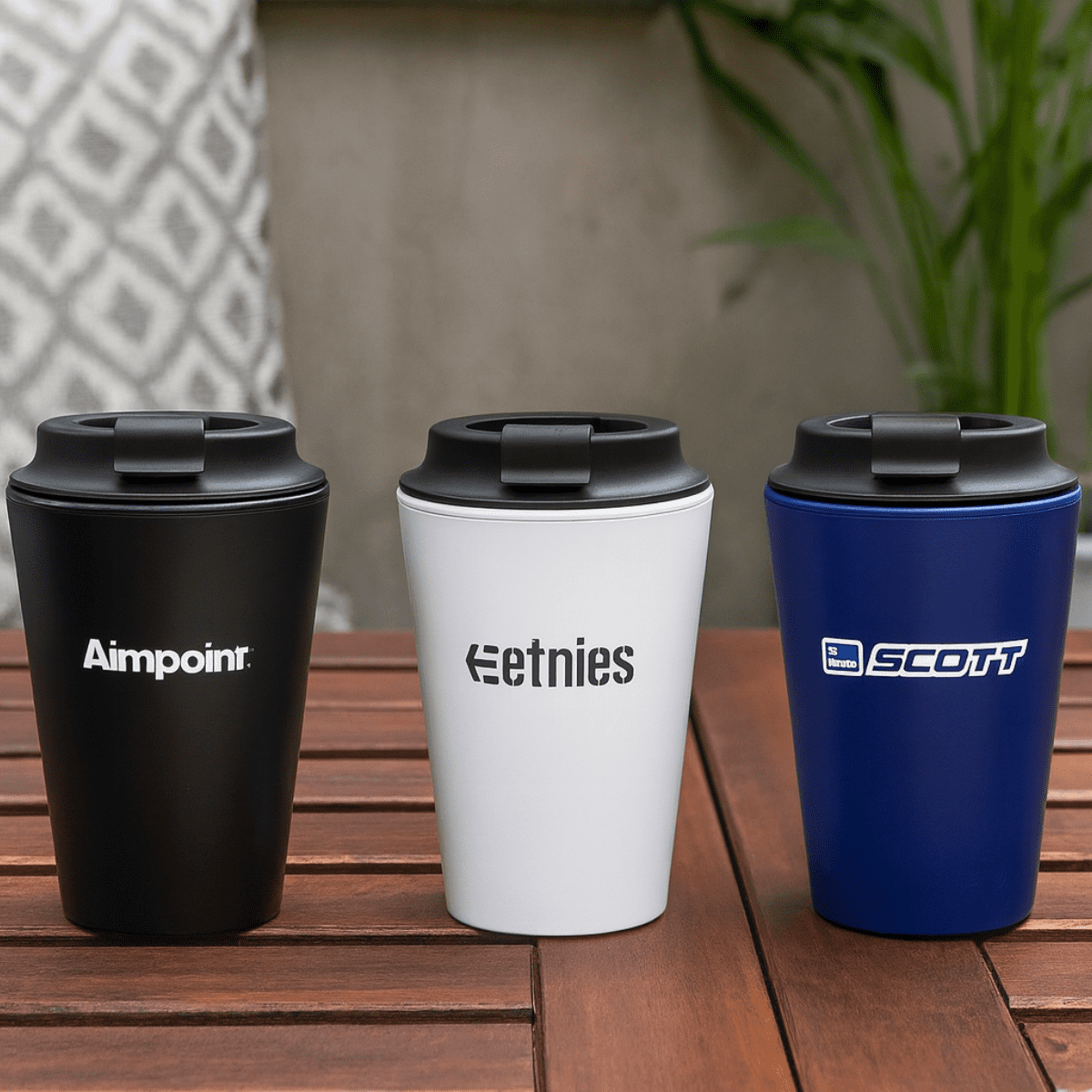Three coffee mugs in black, white, and blue, featuring various logos, placed on a wooden surface. Pacino Recycled PP 350mL Coffee Mug - Image 1