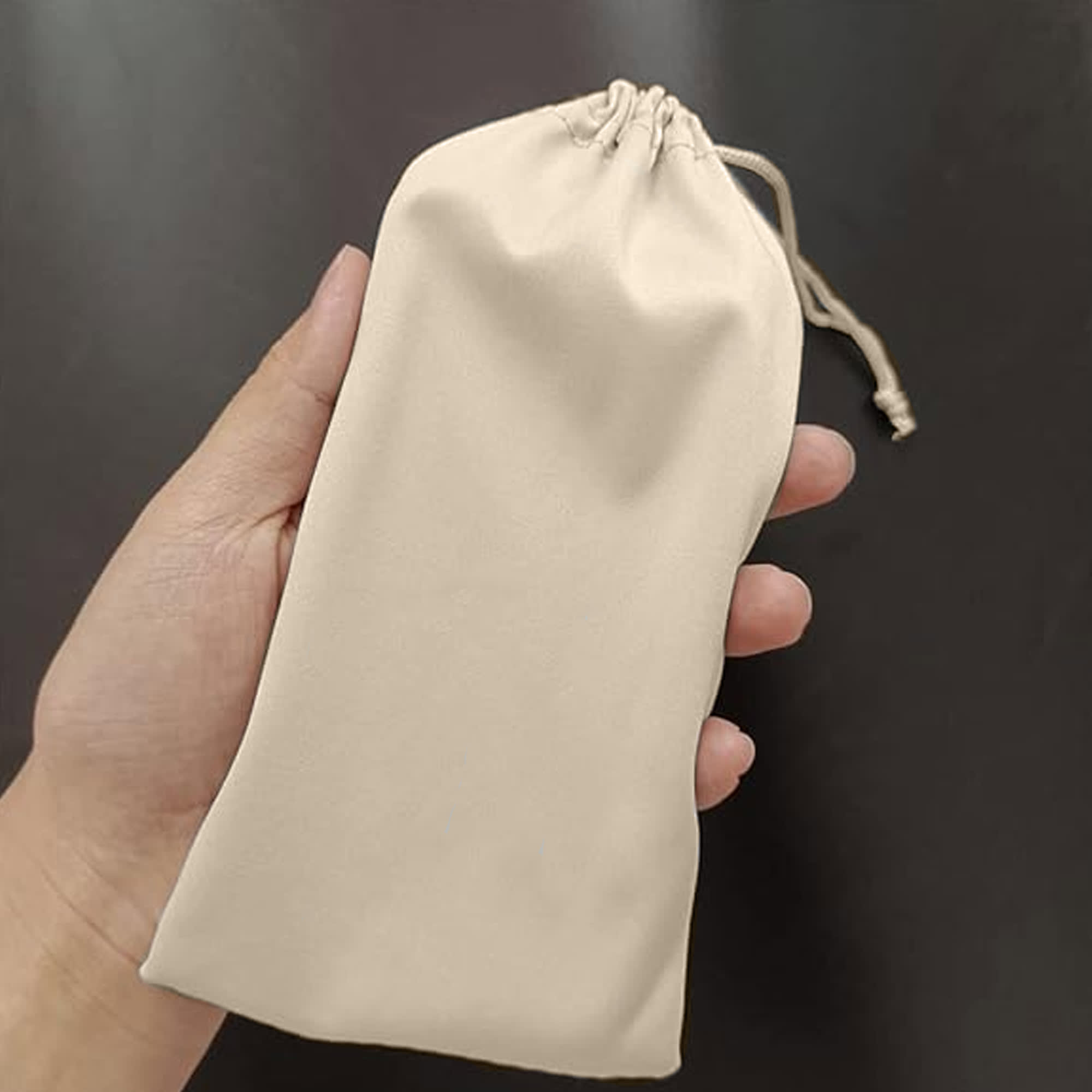 A beige cotton drawstring pouch held in a hand, featuring a cinched top and smooth texture. Cottonfiber Pouch - Image 1