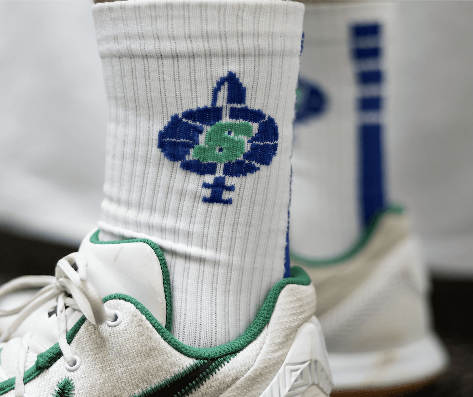 Custom crew-length socks in white with blue and green designs, featuring a logo, worn with athletic shoes. Custom Crew length Socks - Image 1