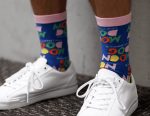 Brightly coloured socks featuring playful graphics and a pink band, worn with white sneakers on a textured surface.