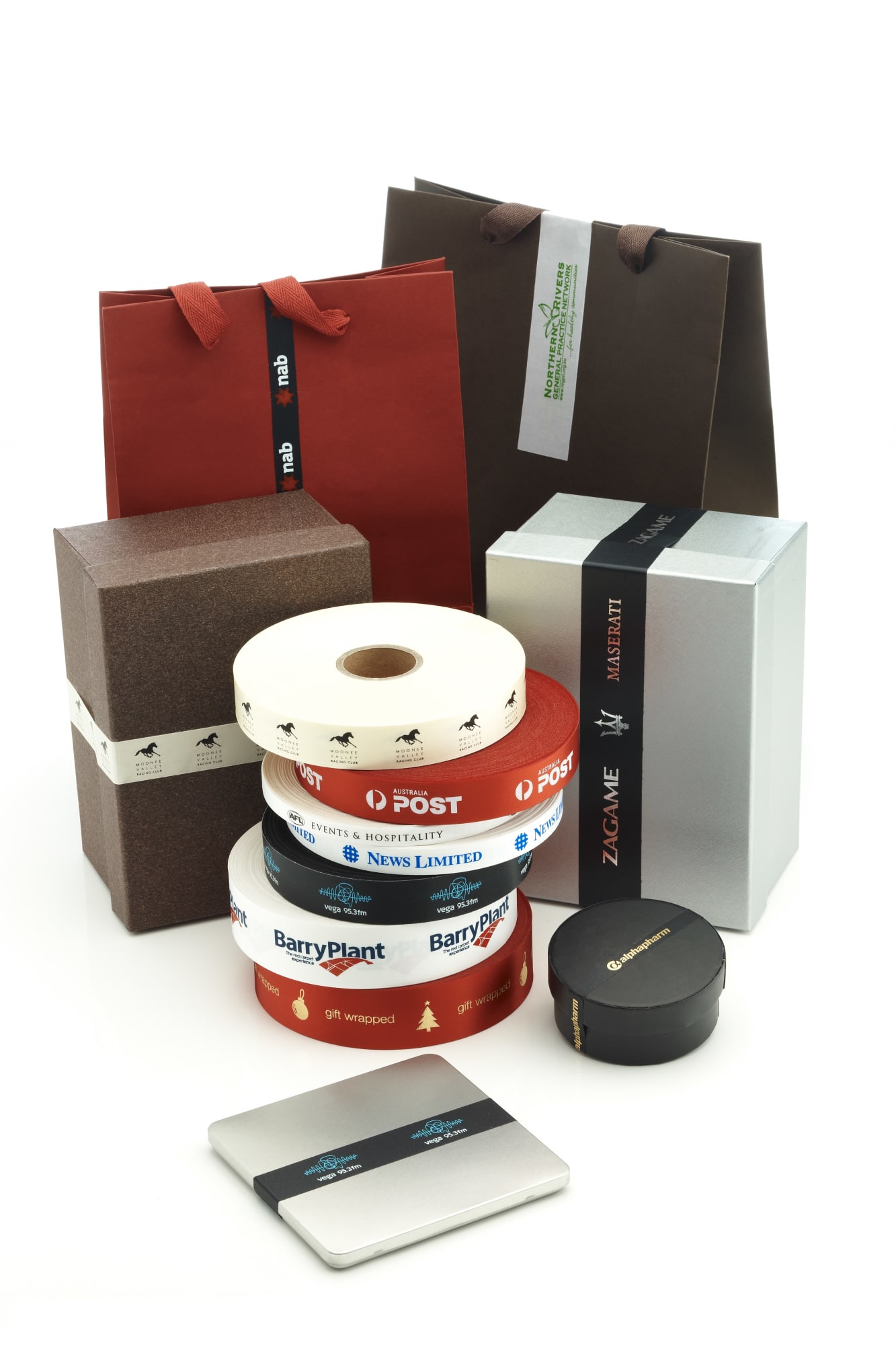 Custom printed satin ribbon in various colours, displayed with gift boxes and shopping bags, some featuring logos. Custom Printed Sticky Backed Satin Ribbon 10mm - Image 1