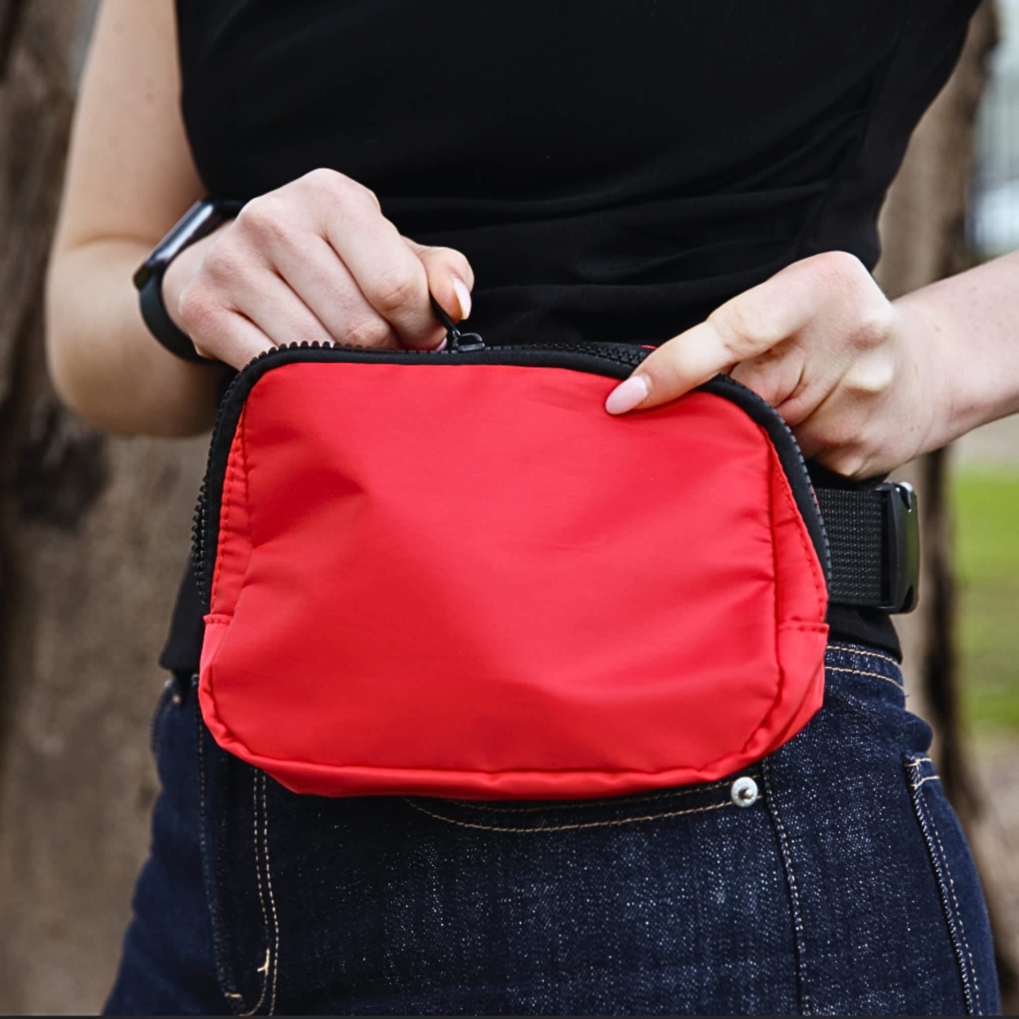 A red bum bag with a black zip, held by a person in a black top, featuring a logo. Go-Mate Belt Bag - Image 1